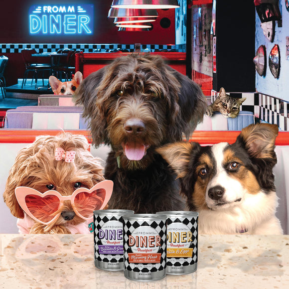 Three dogs in a diner setting with 'Fromm Diner' cans on the table.