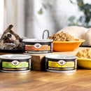 Three cans of animal food on a wooden surface with a blurred background