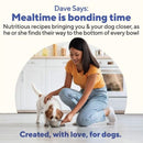 Woman in yellow shirt and blue jeans feeding a dog from a bowl on a kitchen floor.