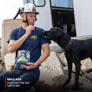 Person in blue shirt and helmet with a black dog, holding Nulo dog food packaging, in front of a vehicle.