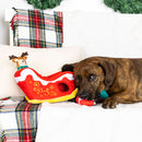 Dog lying on a couch with a Christmas-themed toy and plaid blanket.