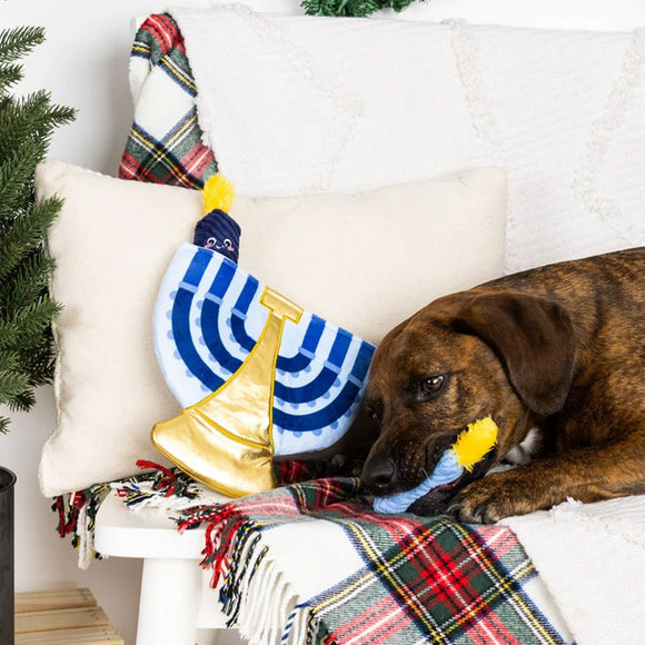 Dog playing with a toy resembling a Hanukkah menorah on a couch with Christmas decorations.