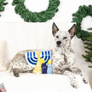 Dog sitting on a couch with a Hanukkah-themed toy in front of Christmas wreaths.