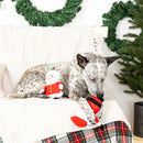 Dog lying on a couch with a Christmas-themed toy, surrounded by festive decorations.