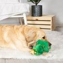 Dog playing with a green Christmas tree toy on a fluffy rug.