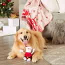 Dog sitting on a wooden floor with a Christmas-themed toy, surrounded by festive decorations.