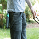 Person holding a garden hose with a device attached, standing outdoors.