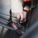 Hand fastening a black seat belt with red branding on a car seat.
