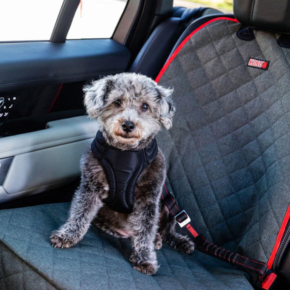Dog sitting on a car seat cover with a visible brand logo.