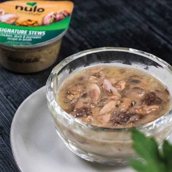 Glass bowl of stew with a container of Nulo pet food in the background