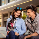 Two people sitting outdoors with a small dog, smiling and enjoying each other's company.