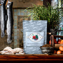 Fromm cat food package on a wooden surface with fish and other items.
