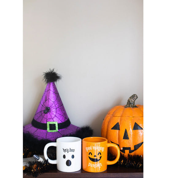 Halloween-themed items including a purple witch hat, white mug with ghost design, orange mug with pumpkin design, and small pumpkin decoration on a shelf.