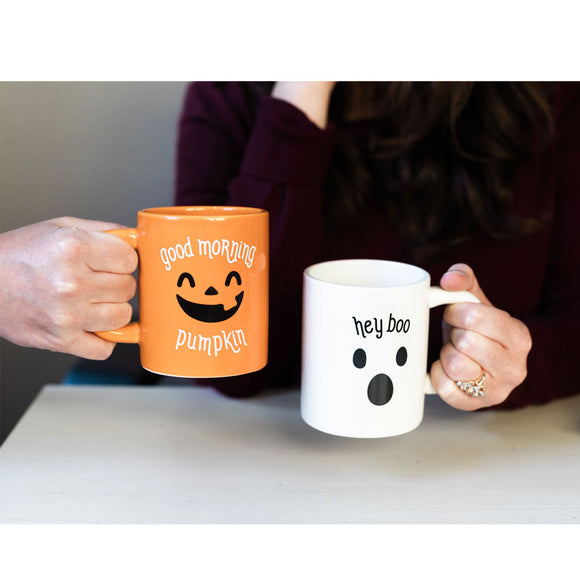 Two mugs with Halloween-themed text and graphics held by two people.
