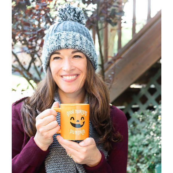 Woman holding an orange mug with a pumpkin design outdoors