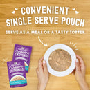 Stella & Chewy's Carnivore Cravings pet food pouches with a bowl of food on a wooden surface.