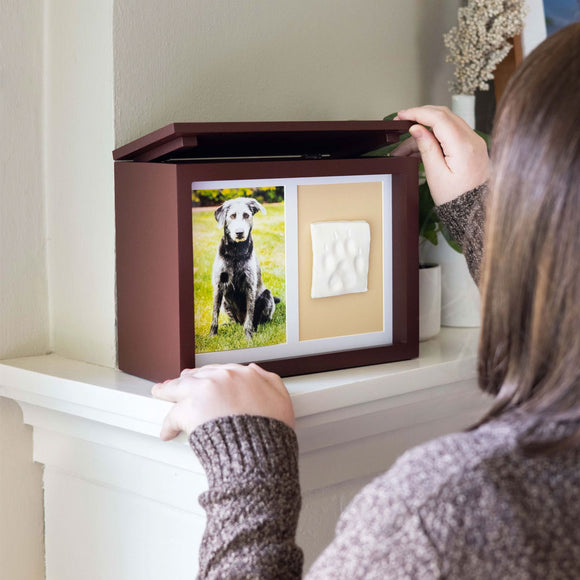 Person interacting with a decorative box featuring a photo of a dog and paw print on a shelf.