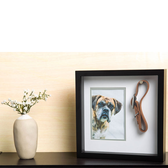 Framed picture of a dog with a leather leash on a shelf next to a vase with flowers.