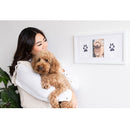Woman holding a dog next to a wall with a framed picture of the dog.