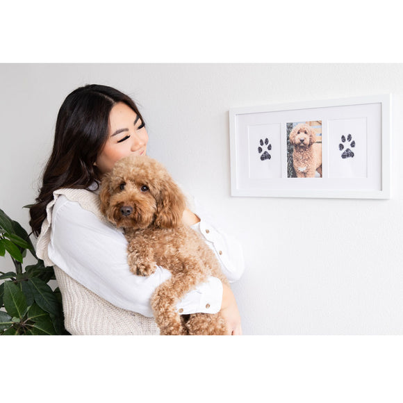 Woman holding a dog next to a wall with a framed picture of the dog.