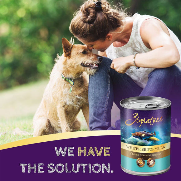 Woman petting a dog with a can of Zignature Whitefish Formula in the foreground, outdoors.