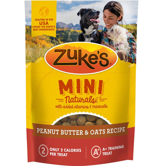 Zuke's Mini Naturals dog treat package with a woman and dog in the background