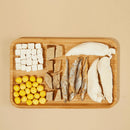 Wooden cutting board with various ingredients including tofu, fish, and lemons on a beige background