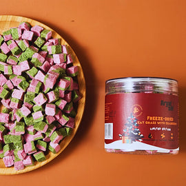 Freeze-dried cat grass with cranberries on a wooden plate next to a red container on an orange background
