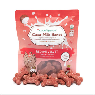 Red velvet dog treats with 'CocoTherapy Coco-Milk Bones' packaging on a white background