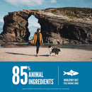 Woman walking a dog on a beach with rocky arches in the background, featuring a product label about animal ingredients.