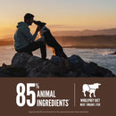 Man and dog sitting on rocks by the ocean at sunset with a product label about animal ingredients.