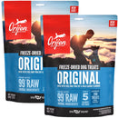 Two packages of Orijen freeze-dried dog treats with a sunset background