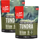 Two packages of Orijen Tundra freeze-dried dog treats with a person and dog in the background.