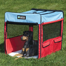 Dog lying inside a red and blue portable pet pen on grass