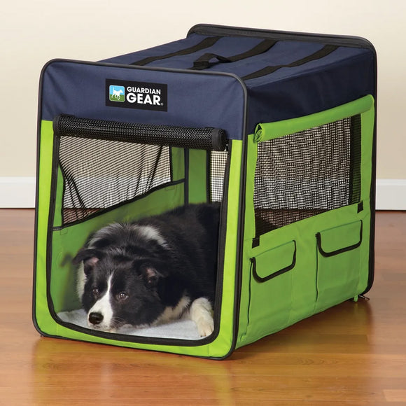 Dog lying inside a green and navy Guardian Gear pet crate on a wooden floor.