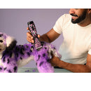 Person grooming a dog with a purple and black pattern using a grooming tool.