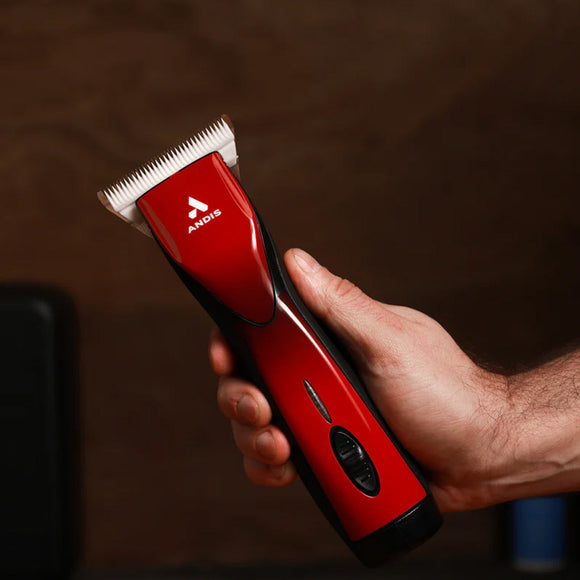 Red Andis hair clipper held in a hand against a dark background