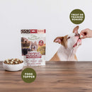 Dog food topper package with a dog eating from a hand on a wooden table.