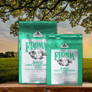 Two packages of Fromm Adult Large & Giant Breed dog food on a wooden surface with a scenic background.