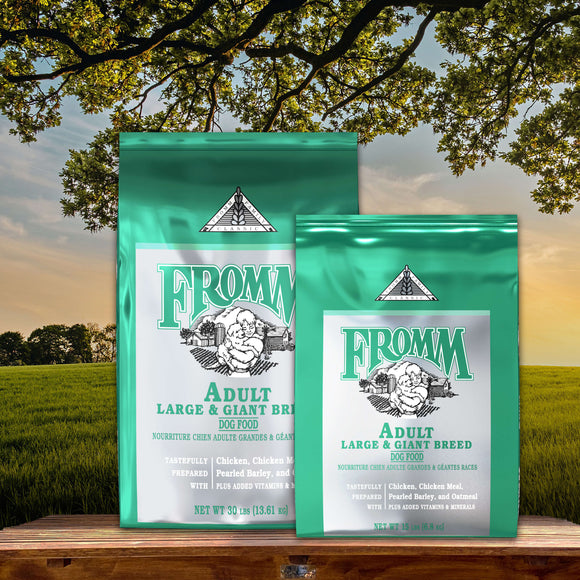 Two packages of Fromm Adult Large & Giant Breed dog food on a wooden surface with a scenic background.