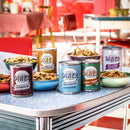 Cans of Diner brand food products on a table with a retro diner setting in the background.